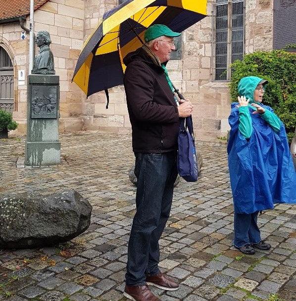 Ein Mann mit Schirm steht vor der Fürther Michaelis-Kirche. Neben ihm gestikuliert eine Frau mit Regenponcho.